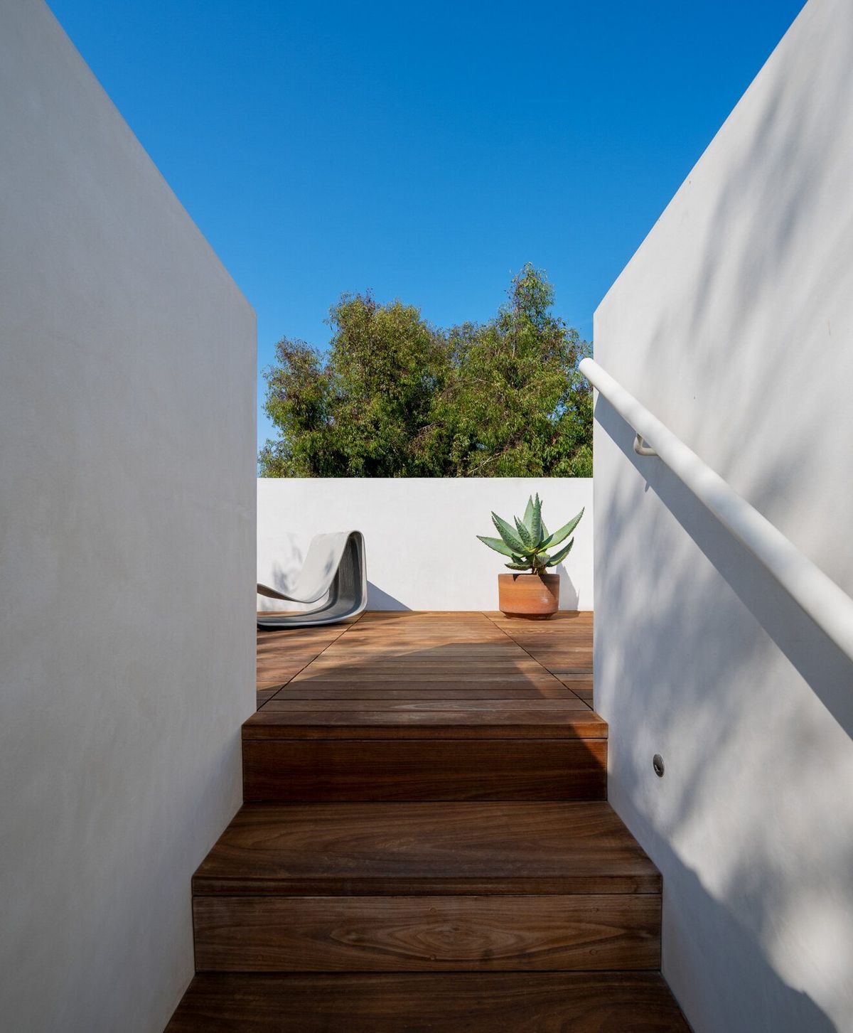 Altair: Wood steps rising between white plaster walls to the roof deck