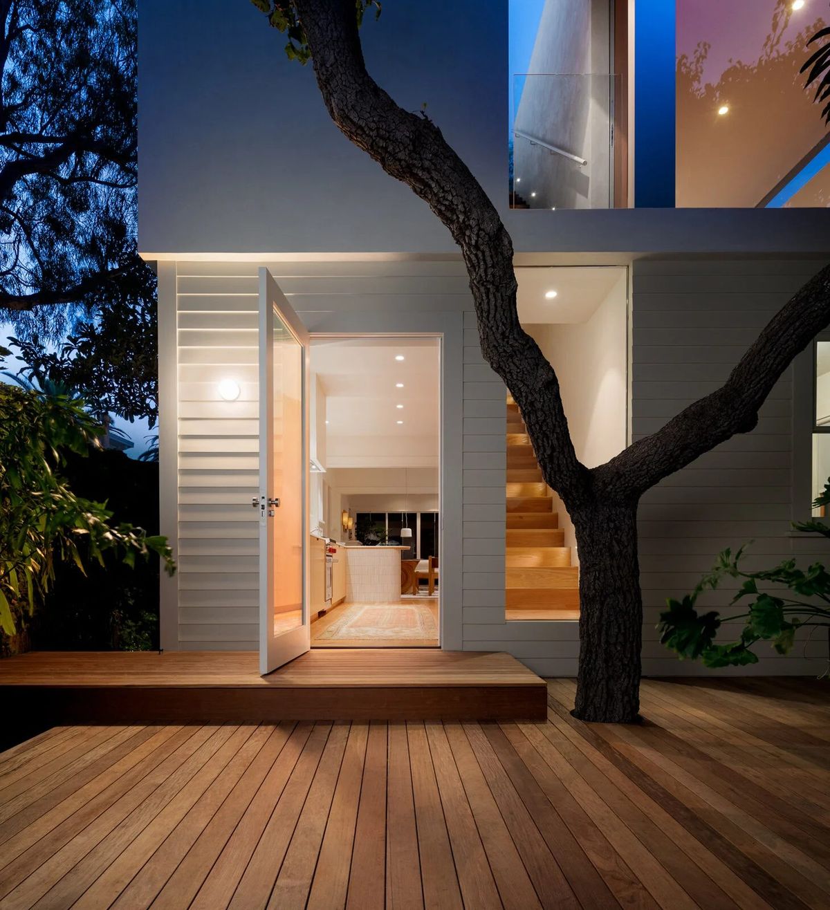 Altair: Addition glowing at dusk over a wood deck, wrapped around the old tree