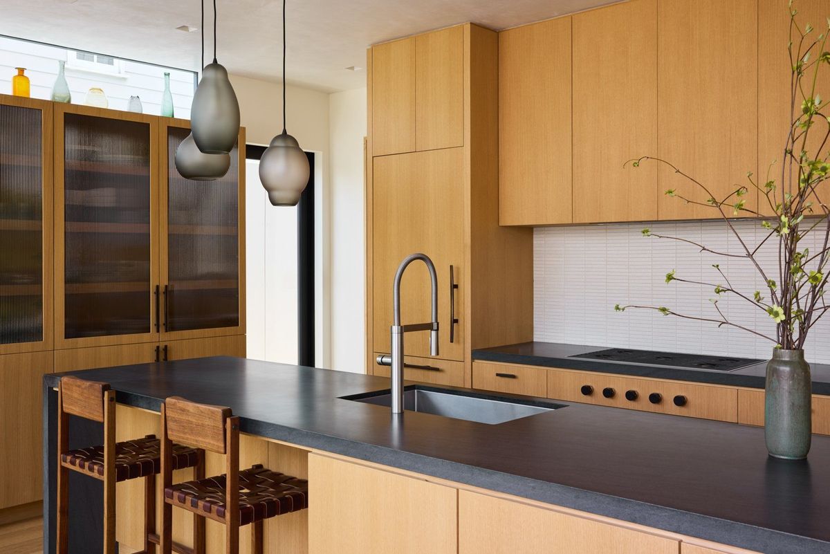 Ashcroft: Kitchen with a dark stone island, oak cabinets and glass pendant lights