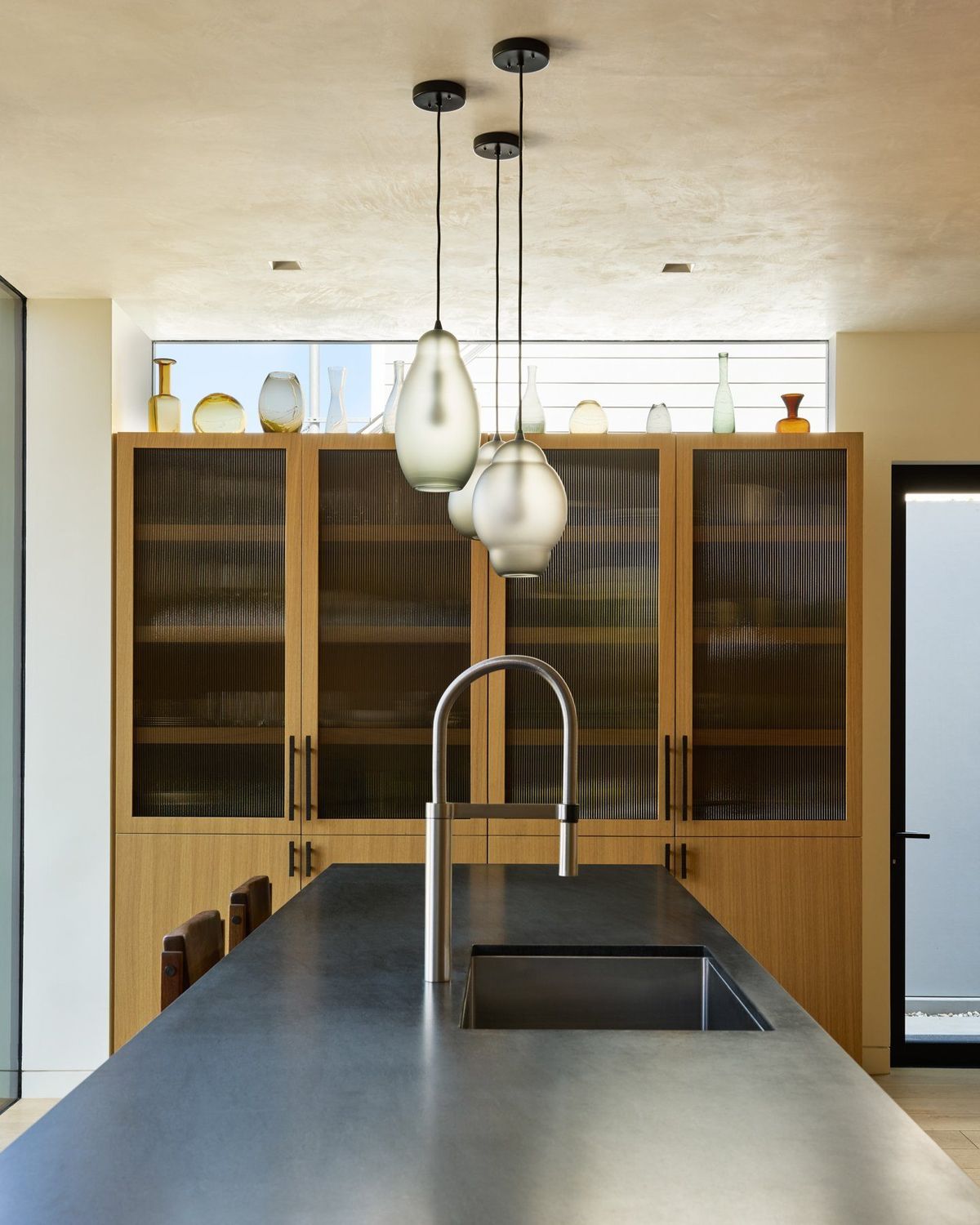Ashcroft: Kitchen island sink under hand-blown glass pendants and fluted glass cabinets