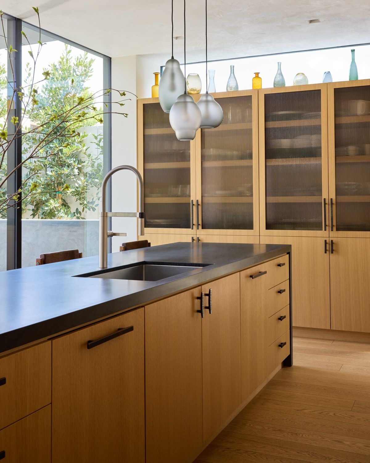 Ashcroft: Oak kitchen with a black countertop and tall glass-front cabinetry