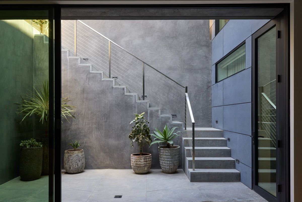 Ashcroft: Concrete stair courtyard with potted plants seen through a black steel door