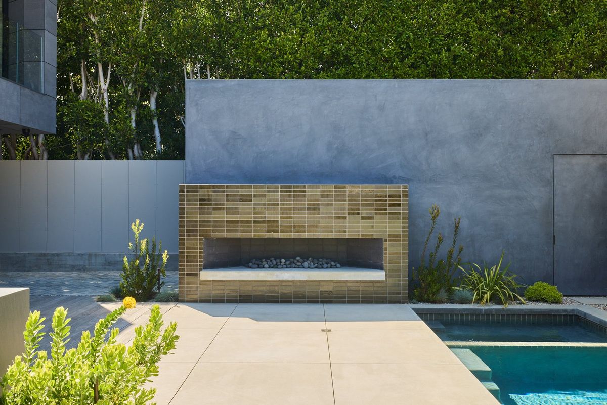 Ashcroft: Backyard with a tiled outdoor fireplace set into a concrete wall beside the pool