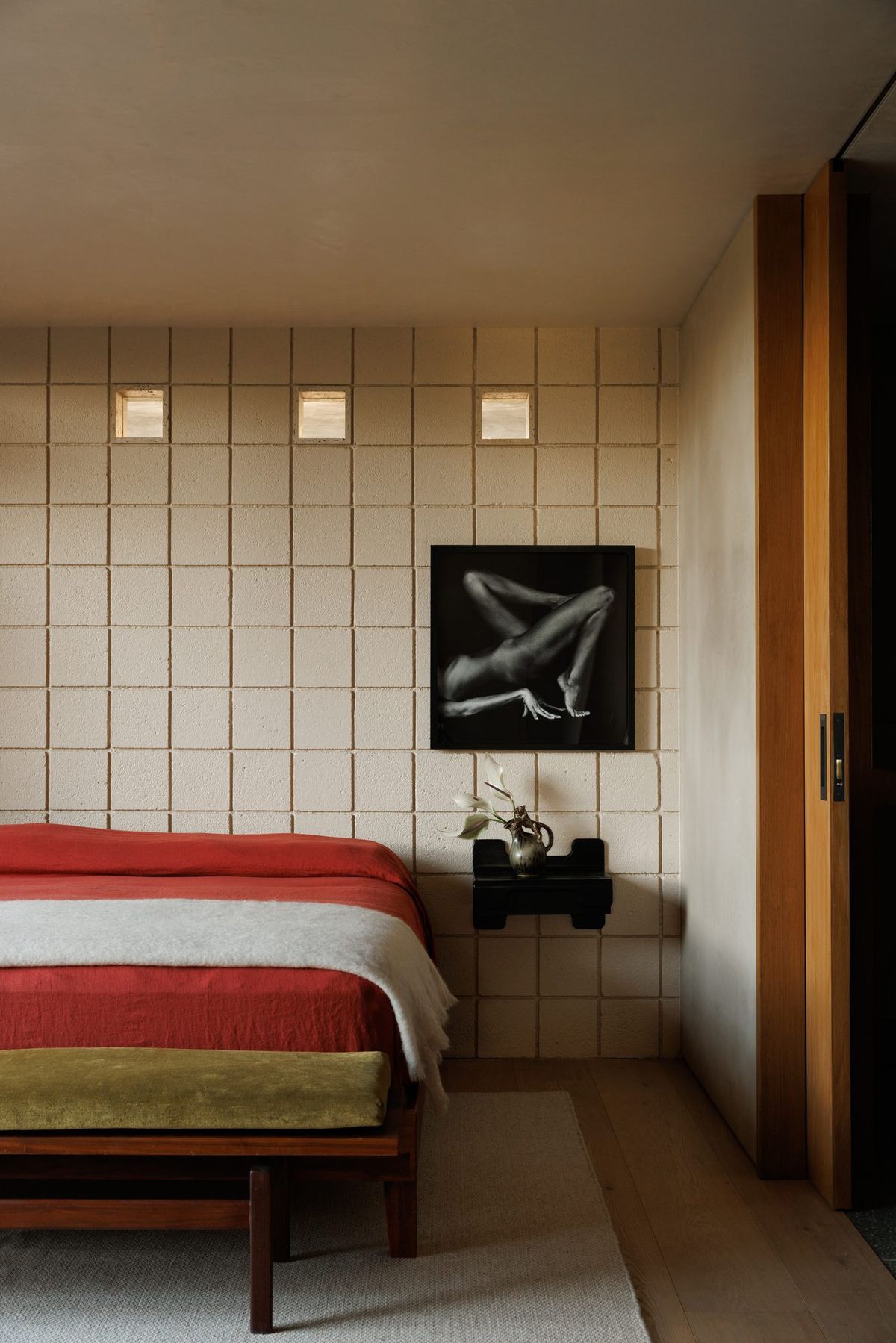 Carla Ridge: Bedroom with a red-striped bed, concrete block wall and framed art