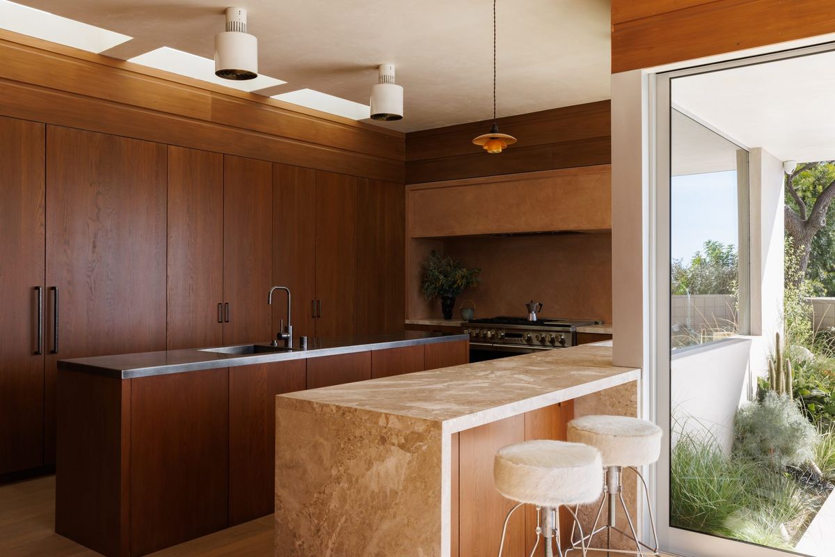 Carla Ridge: Wood-paneled kitchen with a stone waterfall island and white stools