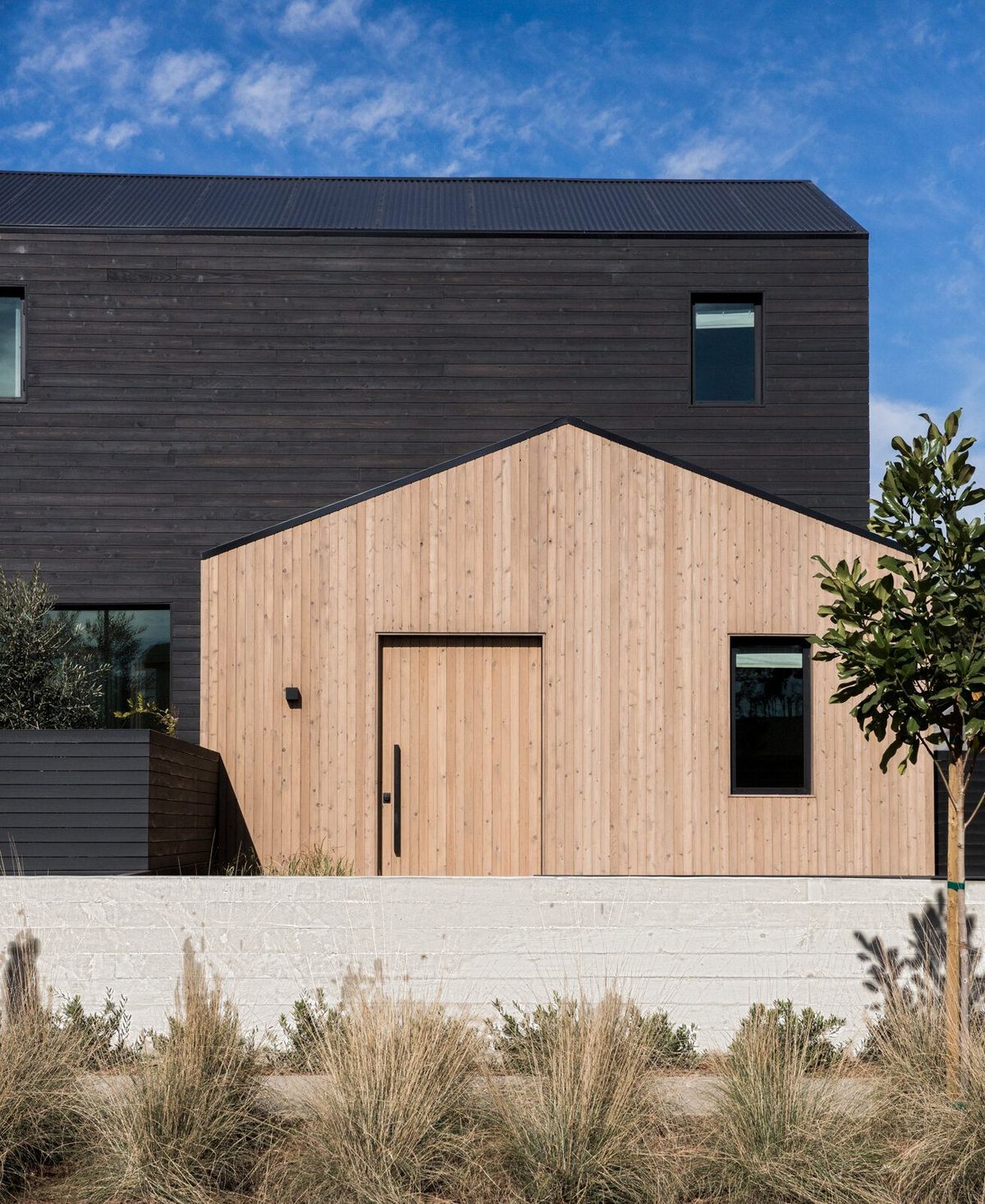 Flower: Modern farmhouse with a wood-clad gable in front of a black-clad two-story volume