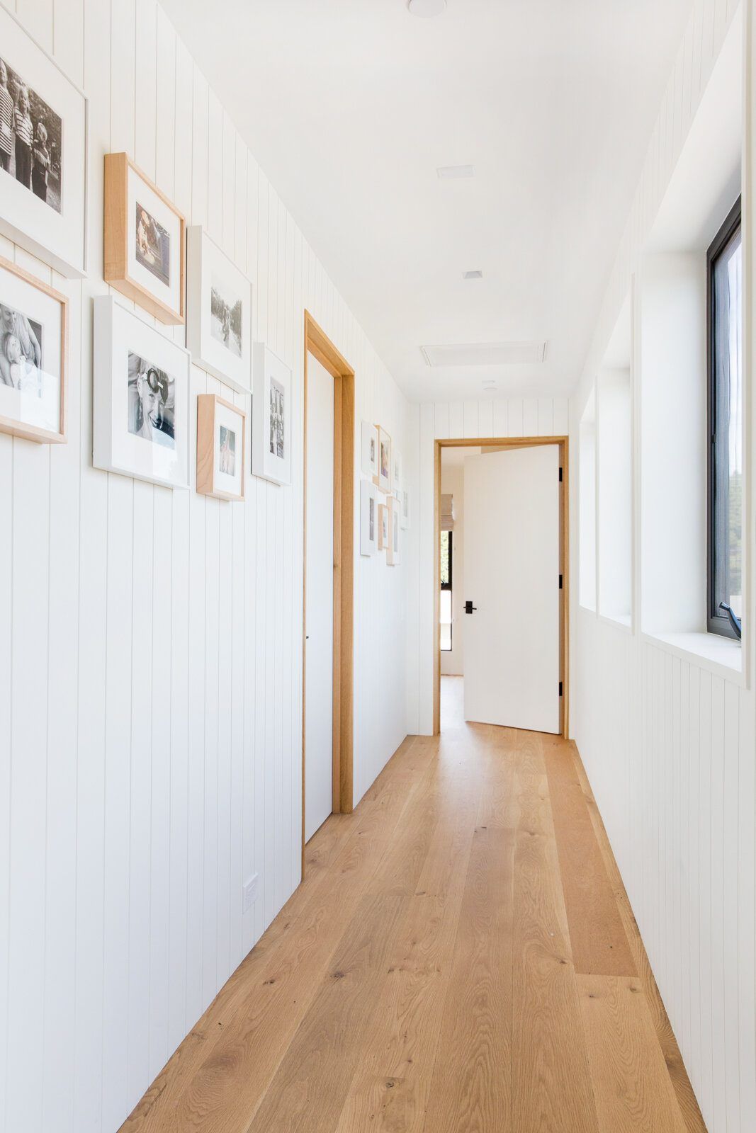Flower: White board-paneled hallway with oak floors and a gallery of frames