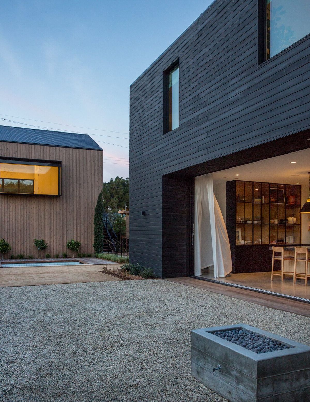 Flower: Black-clad house opening onto a gravel courtyard with a fire pit