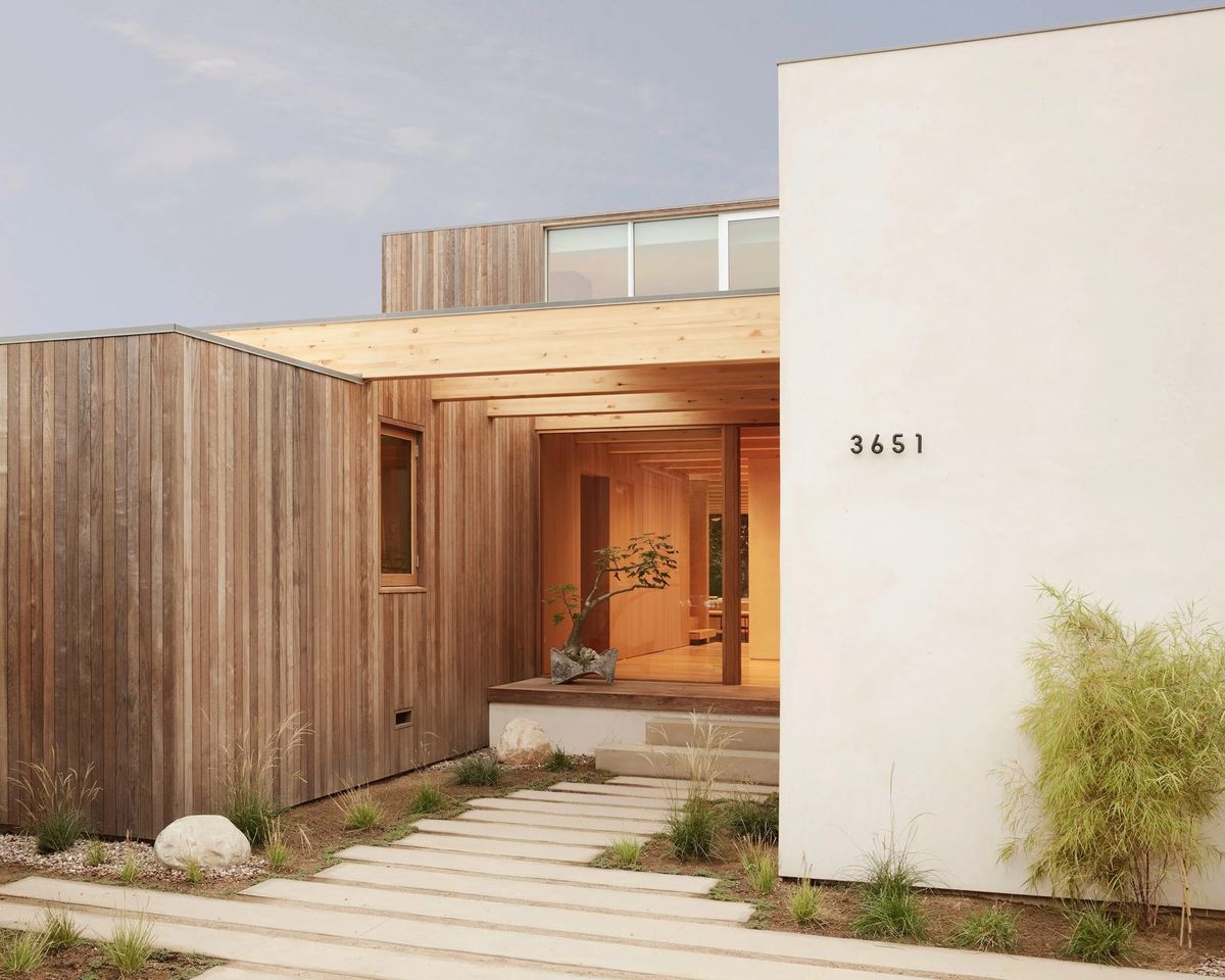 Meier: Street facade of weathered wood cladding beside a white plaster wall numbered 3651