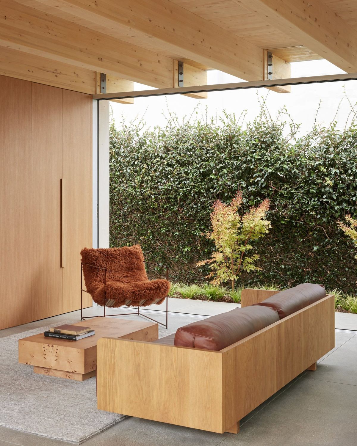 Meier: Sitting area with a wood sofa and leather chair facing a hedge