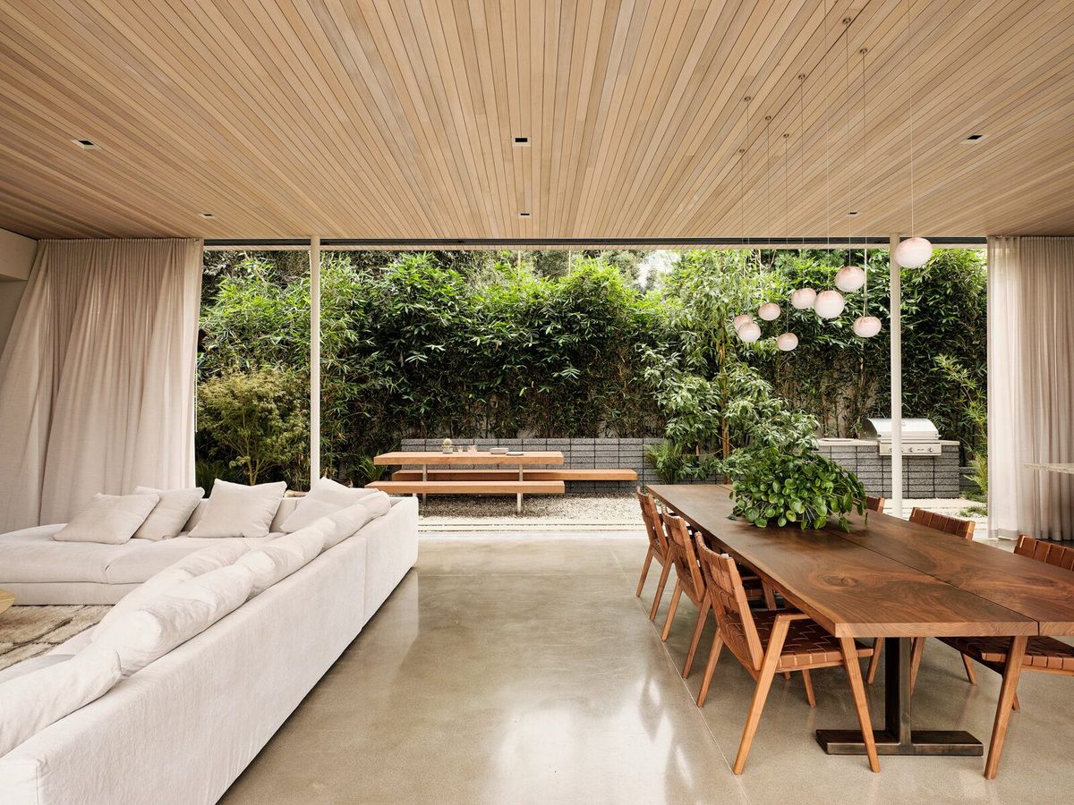 Modjeska: Living and dining room under a wood ceiling, glass walls open to the garden