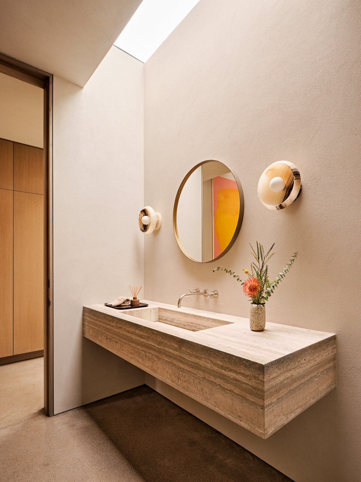 Modjeska: Floating travertine vanity with round mirrors under a skylight
